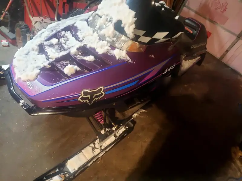 A purple Polaris 440 in the shop with snow still on it.